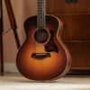 GsMinieRWSB-7 Sunburst acoustic guitar resting on carpet indoors, with a wooden cabinet in the background.