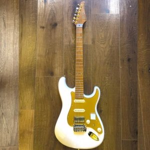 White solid-body electric guitar with a gold pickguard resting on a wooden floor.